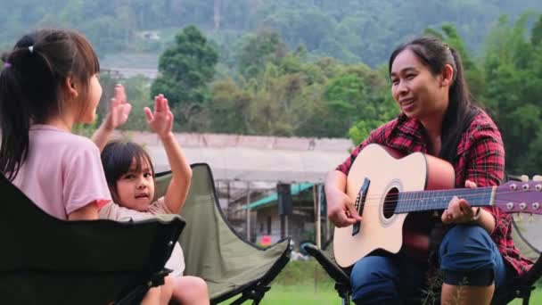 妈妈和孩子们一起弹吉他 在夏令营的帐篷边的椅子上唱歌 一家人在一起度假 — 图库视频影像