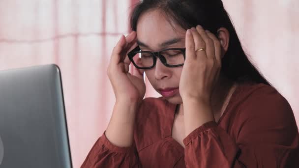 長い間屋内でコンピュータのラップトップで働いていた後 深刻なアジアの女性は頭痛を感じています 健康とオフィス症候群の概念 — ストック動画