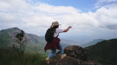 Sırt çantalı bayan yürüyüşçü kollarını kaldırarak dağın tepesinde duruyor ve manzaranın tadını çıkarıyor. yolculuk ve başarı kavramı
