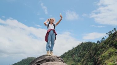 Şapkalı hippi kadın tatilde doğada dinleniyor ve dağ arka planında akıllı telefonuyla selfie çekiyor..