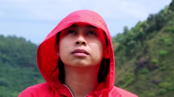 山の上に立つフードに赤い防水ジャケットを着た幸せなアジアの女性ハイカーの肖像画と景色を楽しむ — ストック動画