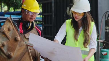 Asian engineering manager and mechanic worker working in a helmet while discussing and inspecting the manufacturing process in the factory.