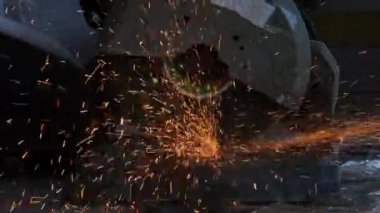 Gözlük ve inşaat eldiveni takan profesyonel adamlar elektrikli çelik kesici makinesiyle ev atölyesinde çalışıyorlar. Metal kesmek kıvılcımları uçurur, yakınlaştırır