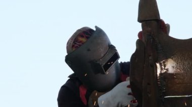 Kaynak maskesi ve eldiven takan yetenekli metal işçileri evde kaynak makinesiyle çalışıyorlar. İşçi metali kıvılcımlarla kaynaştırıyor, yakın plan.