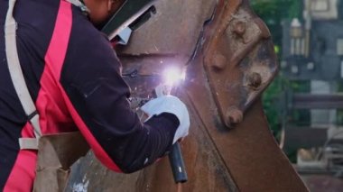 Kaynak maskesi ve eldiven takan yetenekli metal işçileri evde kaynak makinesiyle çalışıyorlar. İşçi metali kıvılcımlarla kaynaştırıyor, yakın plan.