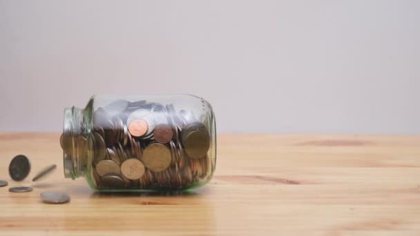 慢慢地 硬币从木制桌子上掉下来的玻璃瓶里滑落了 财务概念 — 图库视频影像