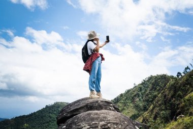 Şapkalı hippi kadın tatilde doğada dinleniyor ve dağ arka planında akıllı telefonuyla selfie çekiyor..