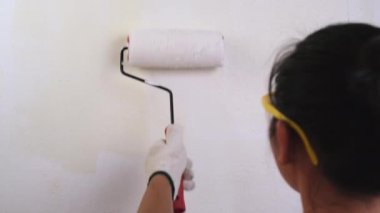 Koruyucu gözlük takan genç bayan dekoratör duvarları silindirle boyuyor. Onarım ve iç dekorasyon.