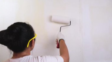 Koruyucu gözlük takan genç bayan dekoratör duvarları silindirle boyuyor. Onarım ve iç dekorasyon.