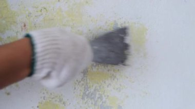 İşçi elinin beton duvara metal bir spatulayla eski boyaları kazıdığı yakın plan. Evdeki duvarların yenilenmesi ve boyanması. bir odayı boyamak için hazırlık