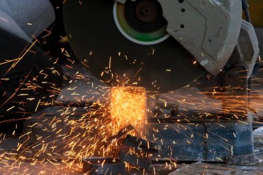 Gözlük ve inşaat eldiveni takan profesyonel adamlar elektrikli çelik kesici makinesiyle ev atölyesinde çalışıyorlar. Metal kesmek kıvılcımları uçurur, yakınlaştırır