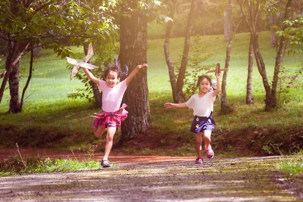快乐的孩子们在夏天的花园里玩纸板飞机 两个带着玩具飞机的妹妹在公园的路上奔跑 快乐童年的概念 — 图库照片