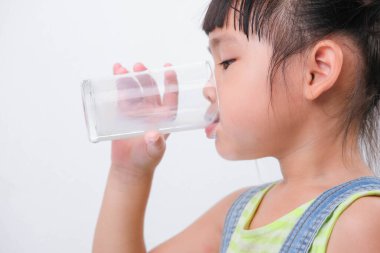 Beyaz arka planda izole edilmiş bir bardaktan süt içen tatlı küçük kız. Küçük kızlar okula gitmeden önce süt içmekten zevk alırlar..