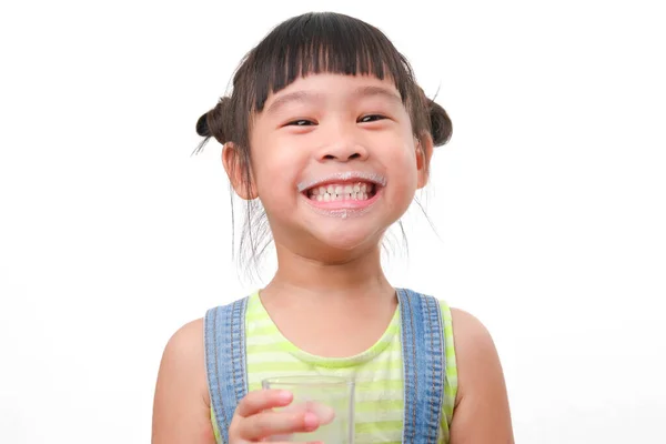 白い背景にミルクのグラスを持った可愛いアジア系の少女の肖像画 笑顔で家にいる小さな女の子 ミルクを飲みながらカメラを見て幸せを感じる — ストック写真