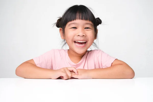 可愛い黒髪の女の子が喜んでピンクの背景にテーブルに座って カメラを見て笑顔 広告子供製品 — ストック写真