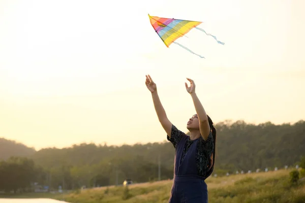 Young woman flying a kite by the lake at sunset.