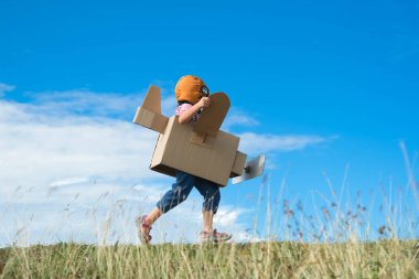 Tatlı hayalperest küçük kız güneşli bir günde çayırda karton uçaklarla oynuyor. Mavi yaz gökyüzü arka planında karton uçakla oynayan mutlu çocuk. Çocukluk hayali kavramı.