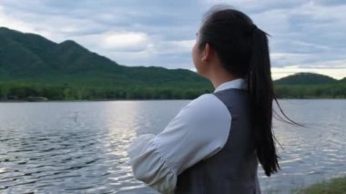 Asyalı kadın gün batımında göl kenarında doğa manzarasının tadını çıkarıyor. Yaşam tarzı ve tatil seyahat kavramı