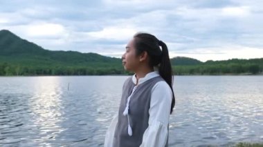 Asyalı kadın gün batımında göl kenarında doğa manzarasının tadını çıkarıyor. Yaşam tarzı ve tatil seyahat kavramı