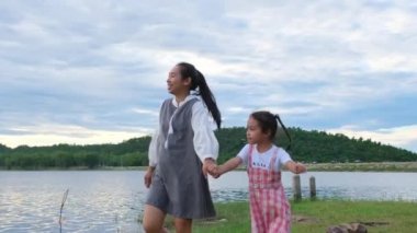 Mutlu anne, göl kenarında birlikte doğanın tadını çıkaran gülümseyen küçük bir kızla el ele yürüyor. Mutlu aile, anne ve küçük kız parkta mutlu mesut oynuyorlar..