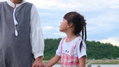 Mutlu anne küçük bir kızla el ele yürür ve göl kenarında birbirine gülümser. Mutlu aile, anne ve küçük kız parkta mutlu mesut oynuyorlar..