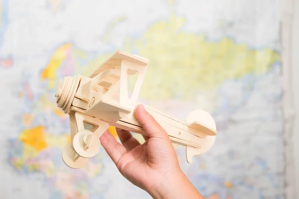 Close-up of wooden toy plane in children\'s hands on world map background in kids room at home. Childhood dream imagination and Travel concepts.