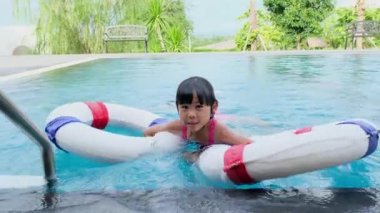 Yüzme havuzunda lastik halkalı mutlu küçük kız kardeşler. Çocuklar yaz tatilinde tropikal tatil yerlerinde açık havuzda oynarlar. Çocuklar yüzmeyi öğreniyor.