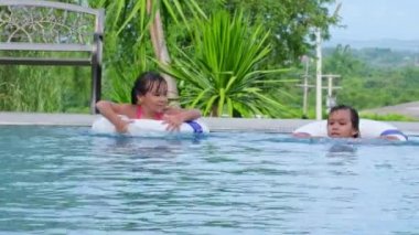 Yüzme havuzunda lastik halkalı mutlu küçük kız kardeşler. Çocuklar yaz tatilinde tropikal tatil yerlerinde açık havuzda oynarlar. Çocuklar yüzmeyi öğreniyor. Çocuklar için Sağlıklı Yaz Faaliyetleri.