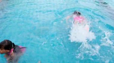Mutlu küçük kız kardeşler yüzüyor ve aile yaz tatili sırasında tropik bir tatil beldesinde açık havuzda oynuyorlar. Çocuklar dalmayı ve yüzmeyi öğreniyor. Çocuklar için Sağlıklı Yaz Faaliyetleri.