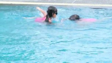 Mutlu küçük kız kardeşler yüzüyor ve aile yaz tatili sırasında tropik bir tatil beldesinde açık havuzda oynuyorlar. Çocuklar dalmayı ve yüzmeyi öğreniyor. Çocuklar için Sağlıklı Yaz Faaliyetleri.