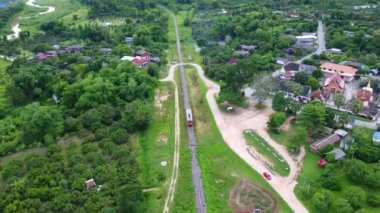 Drone footage of a diesel locomotive passenger train on a rural railroad track moving through a lush tropical forest. Aerial footage of running train through beautiful landscape in Thailand.