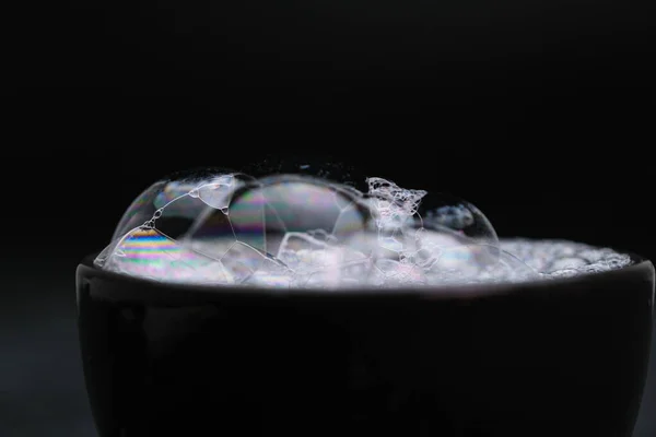 Black cup with foam water and bubbles on black background. Soap bubbles in motion background.