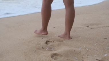 Close up legs of a beautiful woman strolling along the sea looking at the big waves and strong winds. oncept of relaxation and travel on vacation.