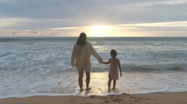 Happy Asian family of mother and daughter having fun playing on the beach during summer vacation at sunset. Summer family trip to the beach. travel and vacation concept.