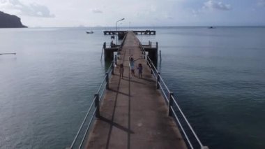 Aerial view from a drone of a happy Asian family of mother and daughters having fun running along the pier in a tropical sea during summer vacation. Travel and vacation concept.