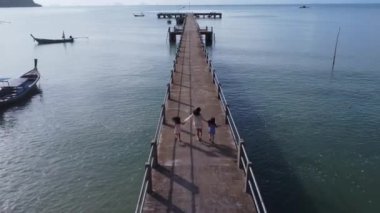Aerial view from a drone of a happy Asian family of mother and daughters having fun running along the pier in a tropical sea during summer vacation. Travel and vacation concept.