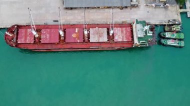 Aerial view from drone of commercial ship with cranes while unloading containers to large commercial ship in the wharf. Transportation and travel background, beautiful sea in summer.