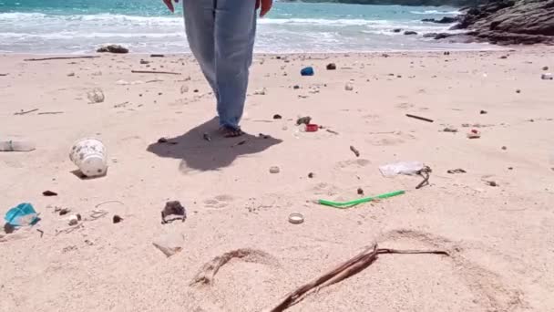 女性はゴミでいっぱいのビーチで裸足で歩き 乾いた小枝とプラスチックで埋め尽くされています 人工物による砂浜の砂の上にゴミをこぼす問題 生態学の概念 — ストック動画