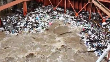 Yağmur mevsiminde kurak dallar ve Kuzey Tayland 'ın kırsal kesimindeki bir baraj kapısındaki plastik atıklarla su taşarken, beton baraj drenaj kanalları tarafından serbest bırakılan kubbeli kahverengi orman suyunun hava manzarası..