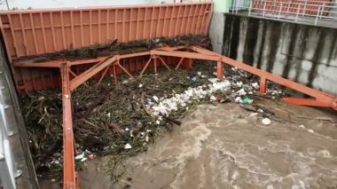 Yağmur mevsiminde kurak dallar ve Kuzey Tayland 'ın kırsal kesimindeki bir baraj kapısındaki plastik atıklarla su taşarken, beton baraj drenaj kanalları tarafından serbest bırakılan kubbeli kahverengi orman suyunun hava manzarası..