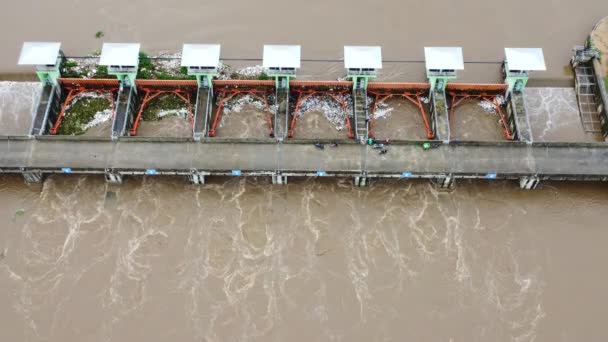 雨季の氾濫としてコンクリートダムの排水路から放出された水の空中ビュー タイ北部の農村部のダムからの濁った茶色の森の水の流れのトップビュー — ストック動画