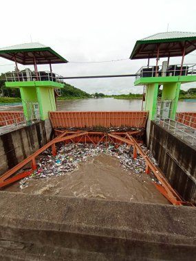 Yağmur mevsiminde kurak dallar ve Kuzey Tayland 'ın kırsal kesimindeki bir baraj kapısındaki plastik atıklarla su taşarken, beton baraj drenaj kanalları tarafından serbest bırakılan kubbeli kahverengi orman suyunun hava manzarası..