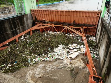 Yağmur mevsiminde kurak dallar ve Kuzey Tayland 'ın kırsal kesimindeki bir baraj kapısındaki plastik atıklarla su taşarken, beton baraj drenaj kanalları tarafından serbest bırakılan kubbeli kahverengi orman suyunun hava manzarası..