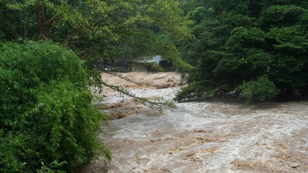 Waterfall cataract in forest mountains. Dirty streams are flowing down the mountain slopes of the mountain forest after heavy rains in Thailand. River flood, selective focus.