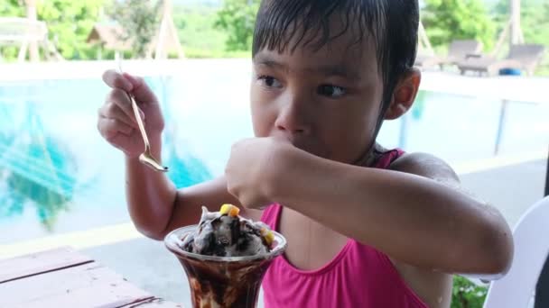 家族の夏休みの間に屋外プールでアイスクリームを食べる水着の小さな女の子 夏のライフスタイルのコンセプト — ストック動画