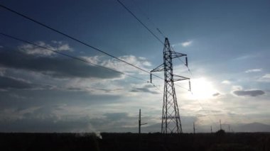 Kırsal kesimde günbatımında gökyüzünde elektrik direklerinin ve kabloların drone görüntüleri. Elektrik direğinin gölgesi alacakaranlıkta.