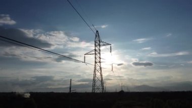 Kırsal kesimde günbatımında gökyüzünde elektrik direklerinin ve kabloların drone görüntüleri. Elektrik direğinin gölgesi alacakaranlıkta.