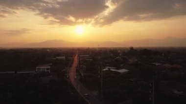 Güneşin altın ışıklarıyla gün batımı gökyüzü arkadaki dağ manzaraları ve kırsal köylerin siluetlerine karşı. Gün batımında kırsalda bulutlu ve güneşli güzel gökyüzü manzarası.