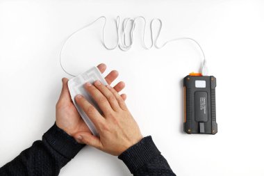 Eller, beyaz arka planda güç bankasına bağlı taşınabilir USB ısıtıcıyı tutuyor