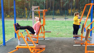 İki tombul kız sokak simülatörleri üzerinde spor egzersizleri yapıyor, sağlıklı bir yaşam tarzı için motivasyon.